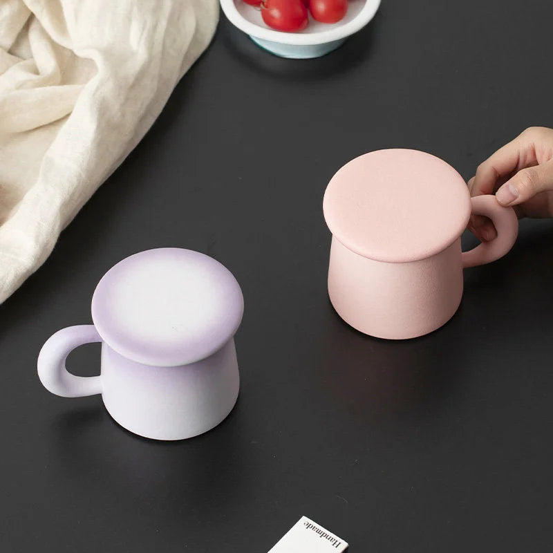 Two Frosted Ceramic Mugs, Lavender Ombre and Dusty Pink, with lids on a black surface - RoomDen.