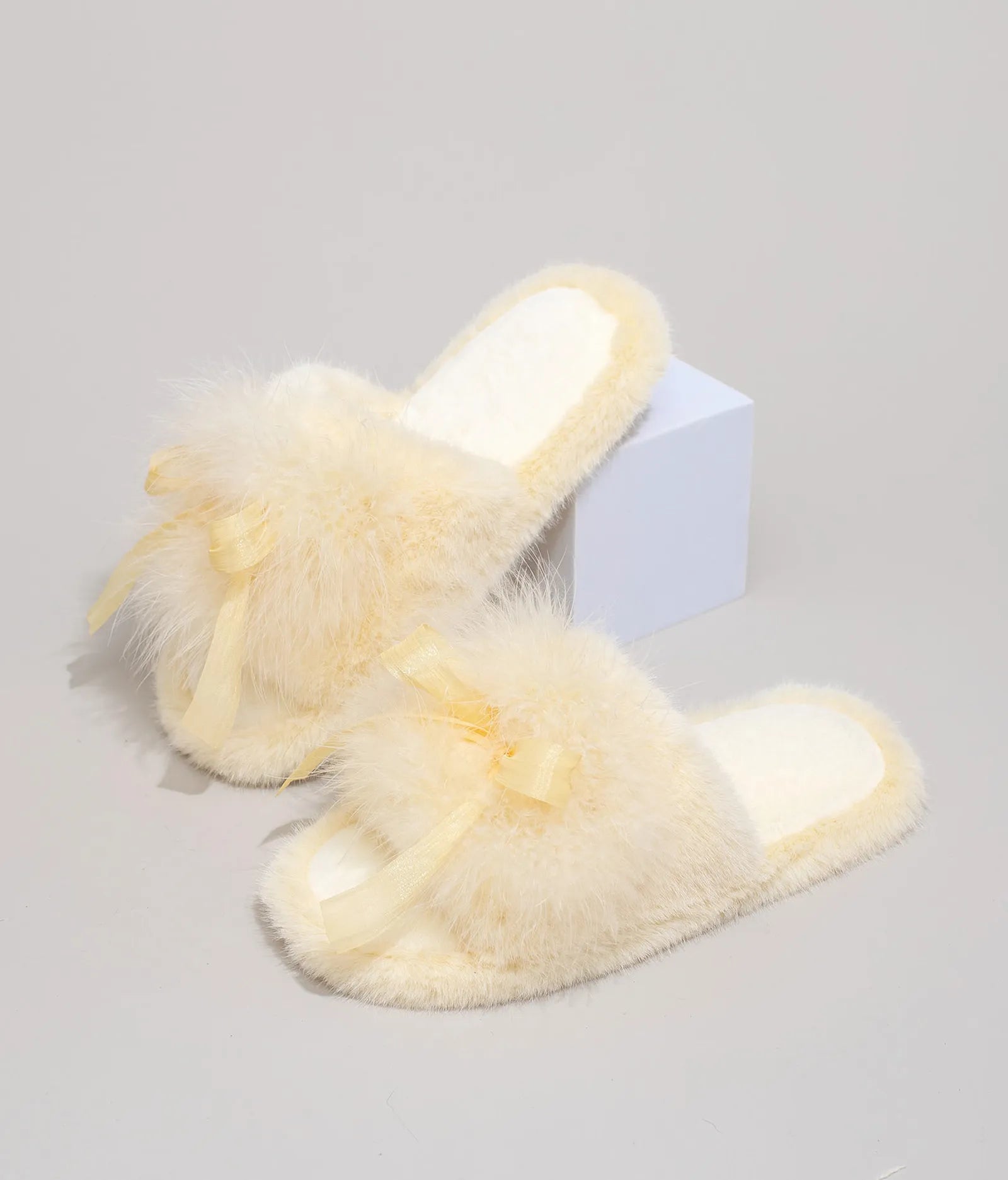 Butter Yellow plush bedroom slippers with satin bow accent on white prop - RoomDen