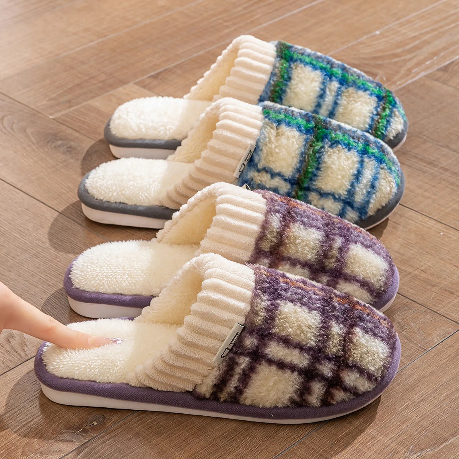 Three pairs of plush plaid sherpa house slippers in brown, purple, and green lined up on a wooden floor - RoomDen