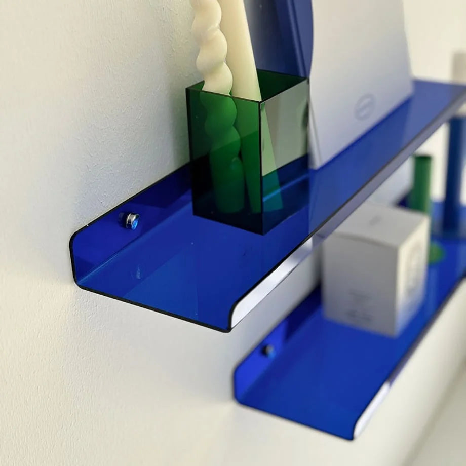 Detail shot of the glossy surface of the blue floating shelf holding a green candle holder and a book.