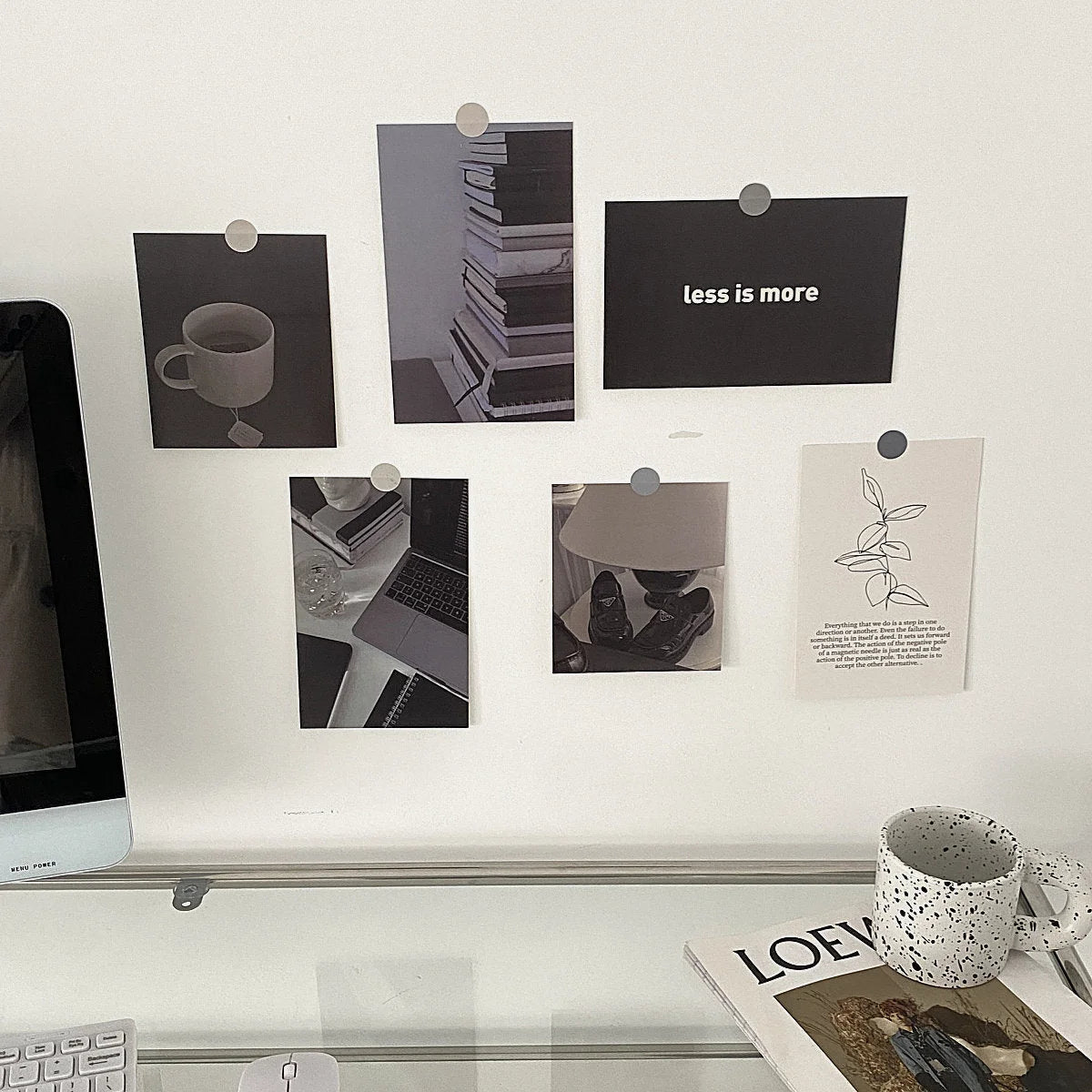 Black and white wall collage kit pinned to a white wall above a clean, modern desk with a computer and magazines. - RoomDen