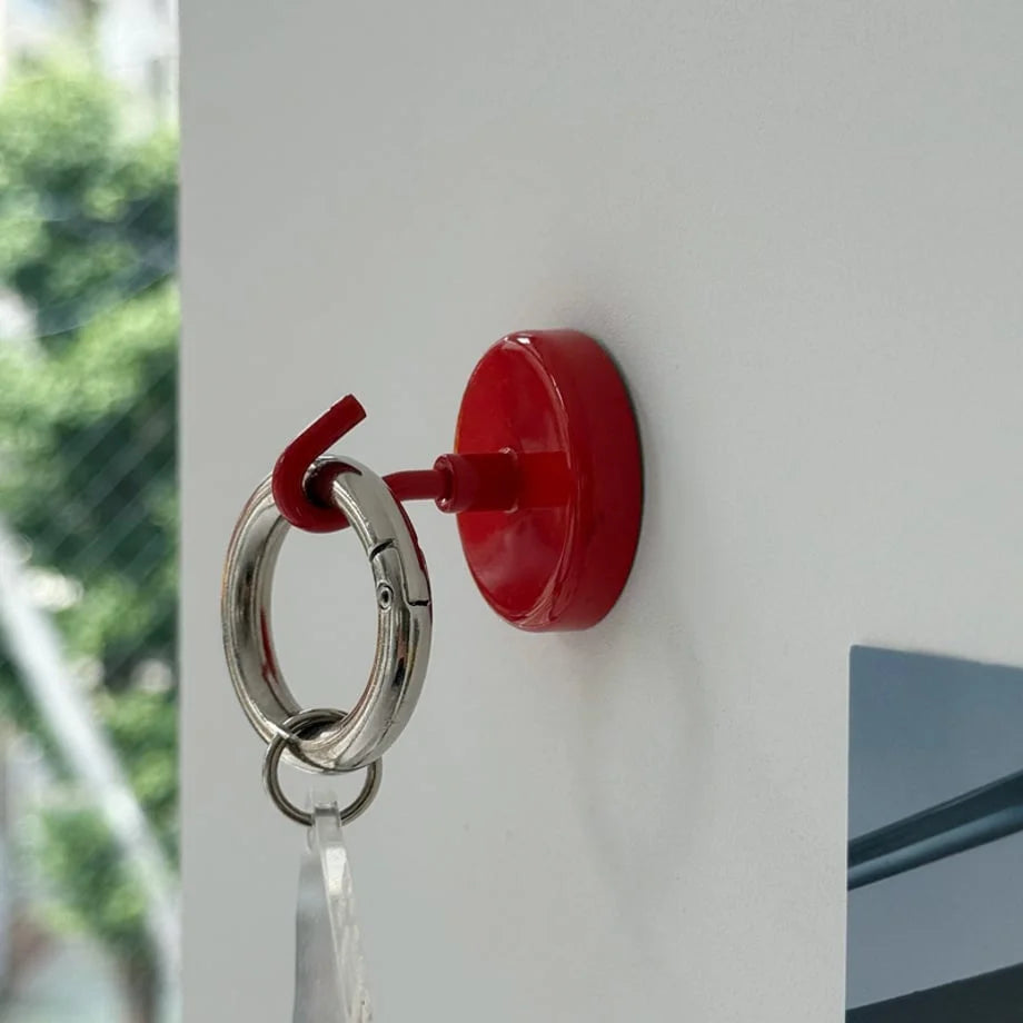 Detailed view of a red magnetic metal hook holding a silver keychain ring against a white wall - RoomDen