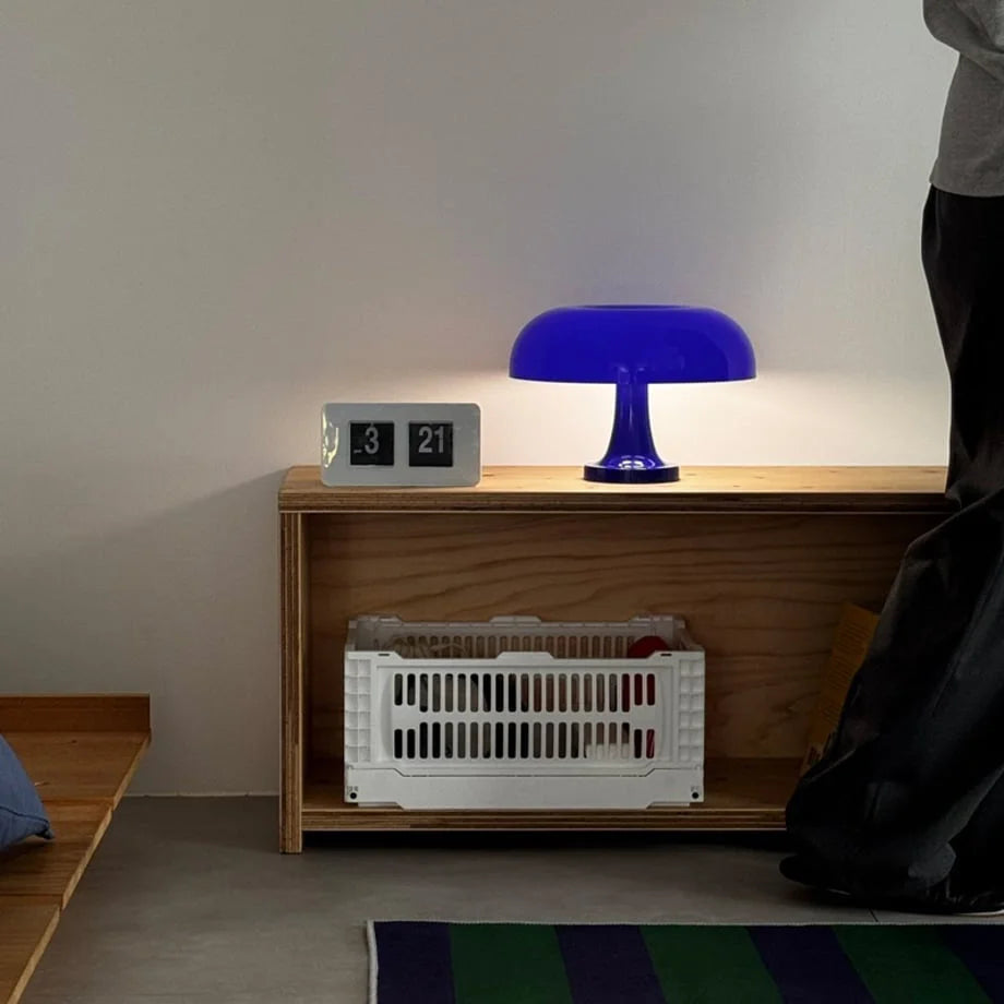 Cobalt blue mushroom lamp glowing on a plywood bookshelf next to a flip clock - RoomDen.