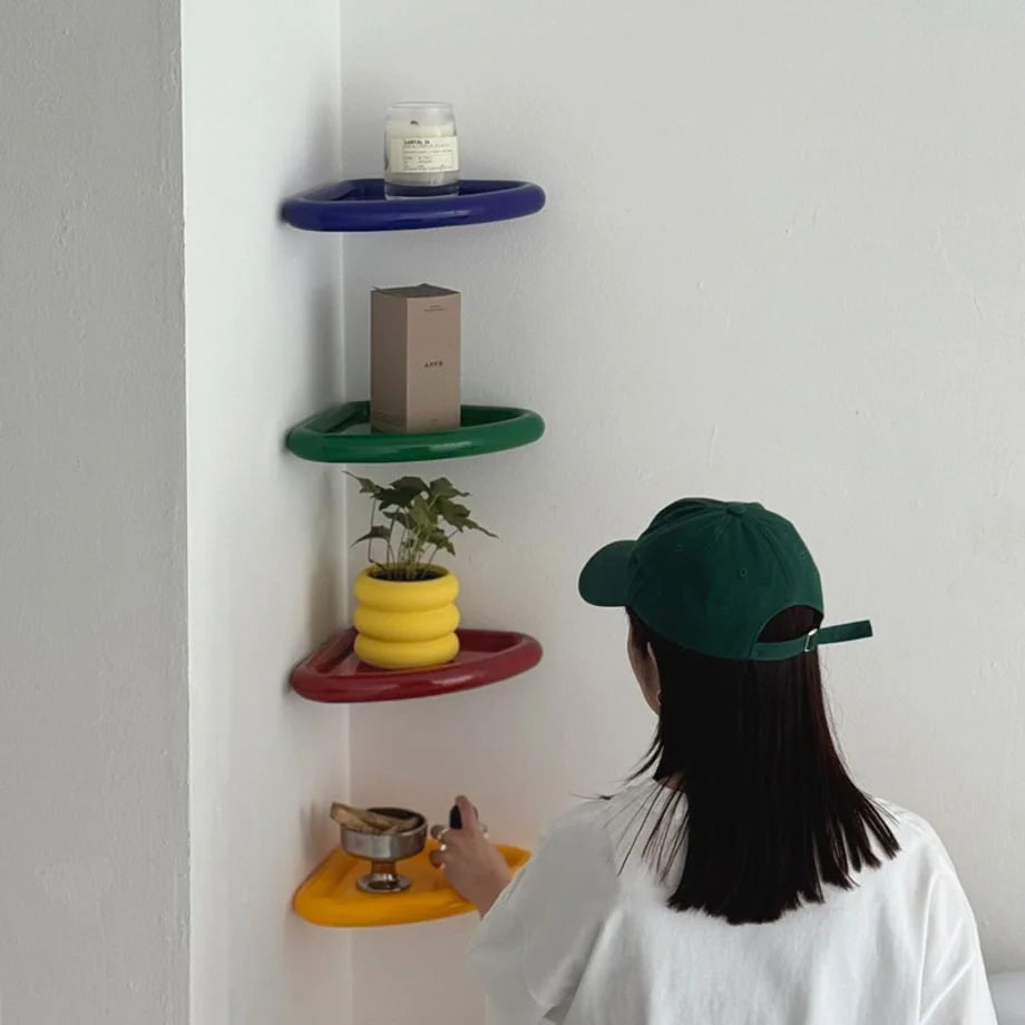 A person in a green cap arranging items on a set of colorful floating corner shelves in a bright white room. - RoomDen