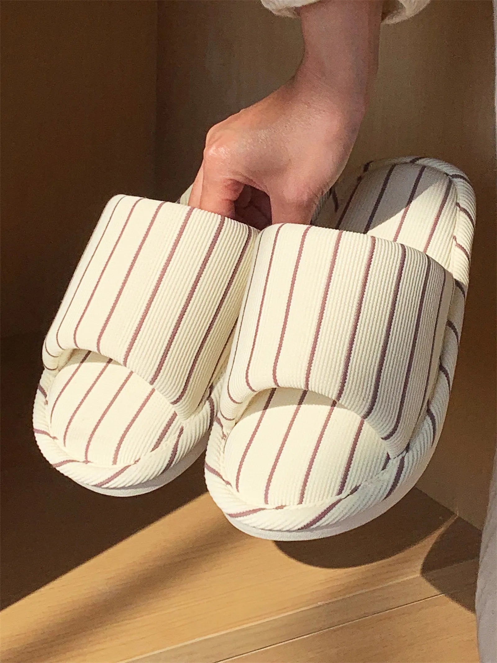 Hand holding a pair of Beige & Brown Striped slippers to demonstrate the lightweight and flexible sole construction.