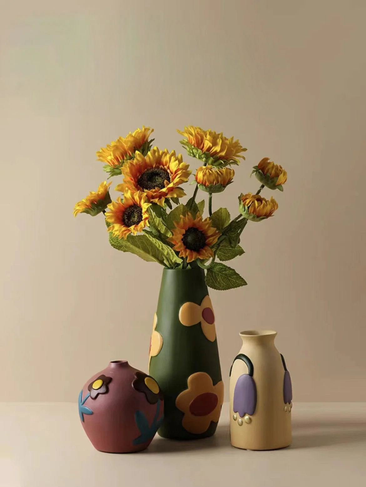 Lifestyle shot of three Pop Art Floral Ceramic Vases (green, mauve, beige) with a bouquet of sunflowers. - RoomDen