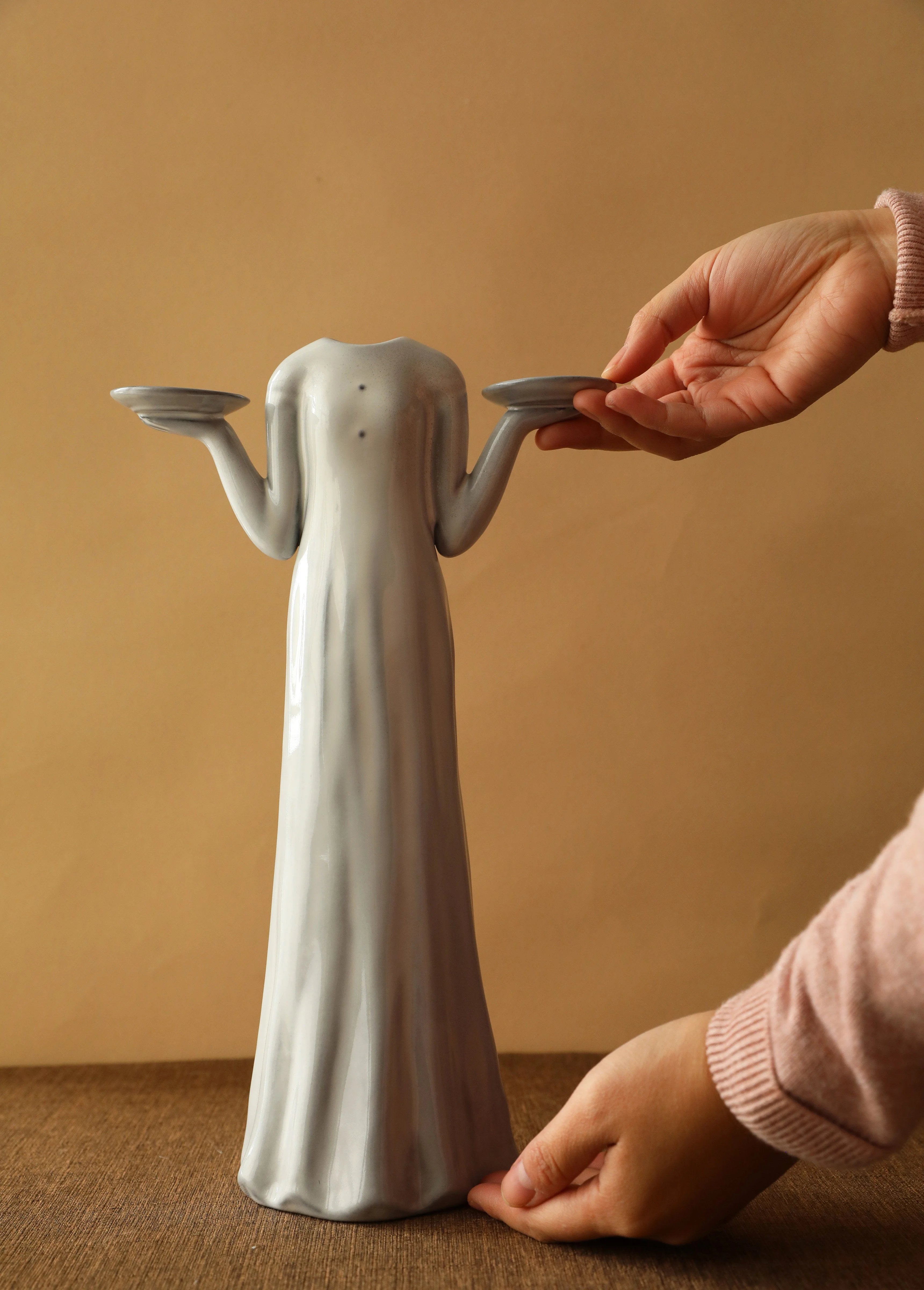 A hand adjusting the tall female figure ceramic vase, designed to hold candles or flowers. - RoomDen