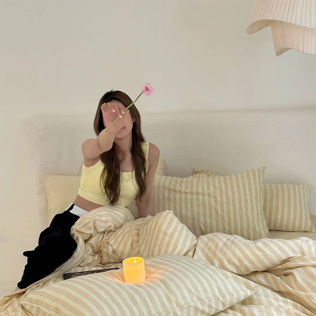 Model Sitting on Bed with Yellow Striped Duvet Cover Holding Flower - RoomDen