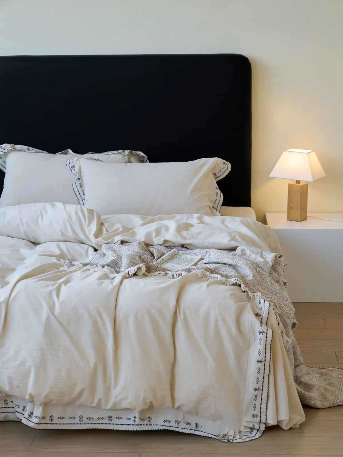 Front view of cream embroidered linen bedding set with black headboard RoomDen.