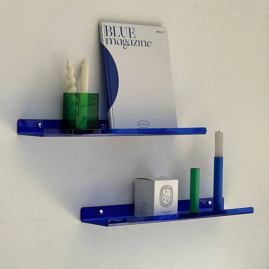 Main image of the Sleek Minimalist Acrylic Floating Shelf in vibrant blue, displaying a magazine and candles against a white wall - RoomDen.