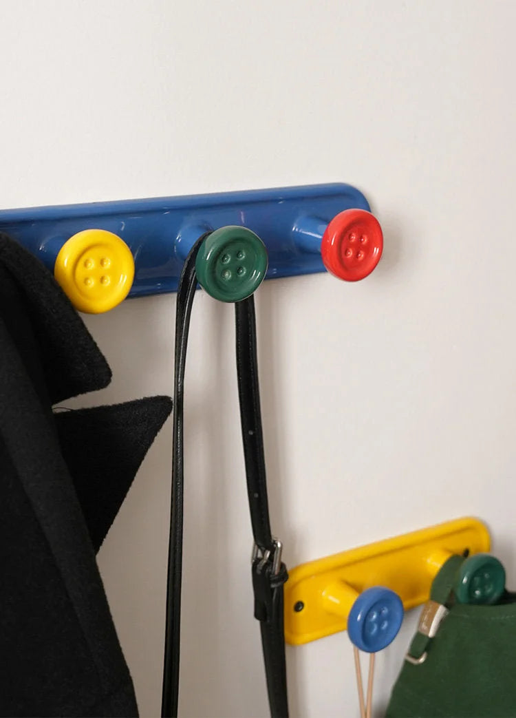 Lifestyle view of blue and yellow button wall hooks holding a black coat and a purse. - RoomDen