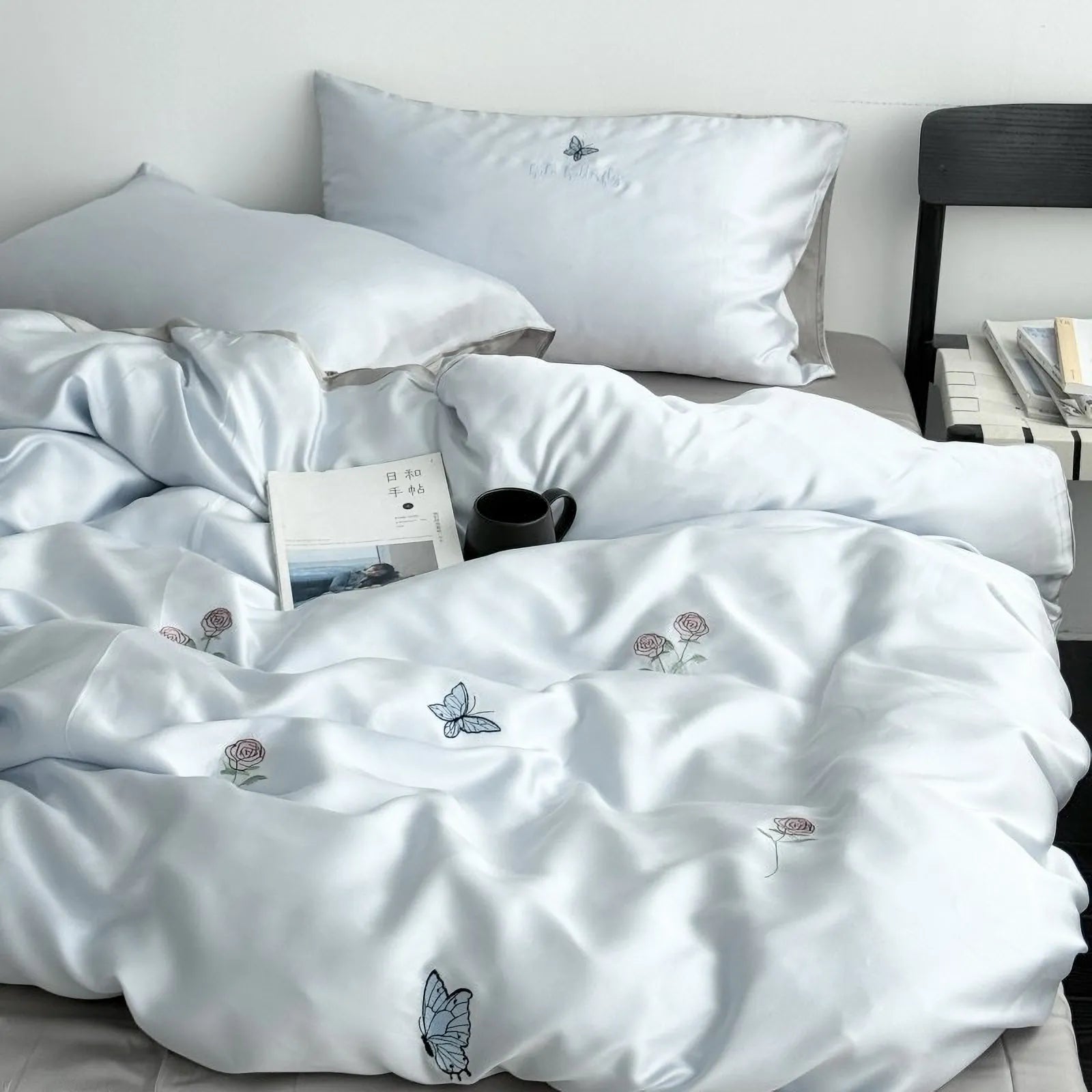 Main lifestyle shot of the Cloud Blue embroidered butterfly and rose Tencel bedding set, neatly made on a bed. - RoomDen
