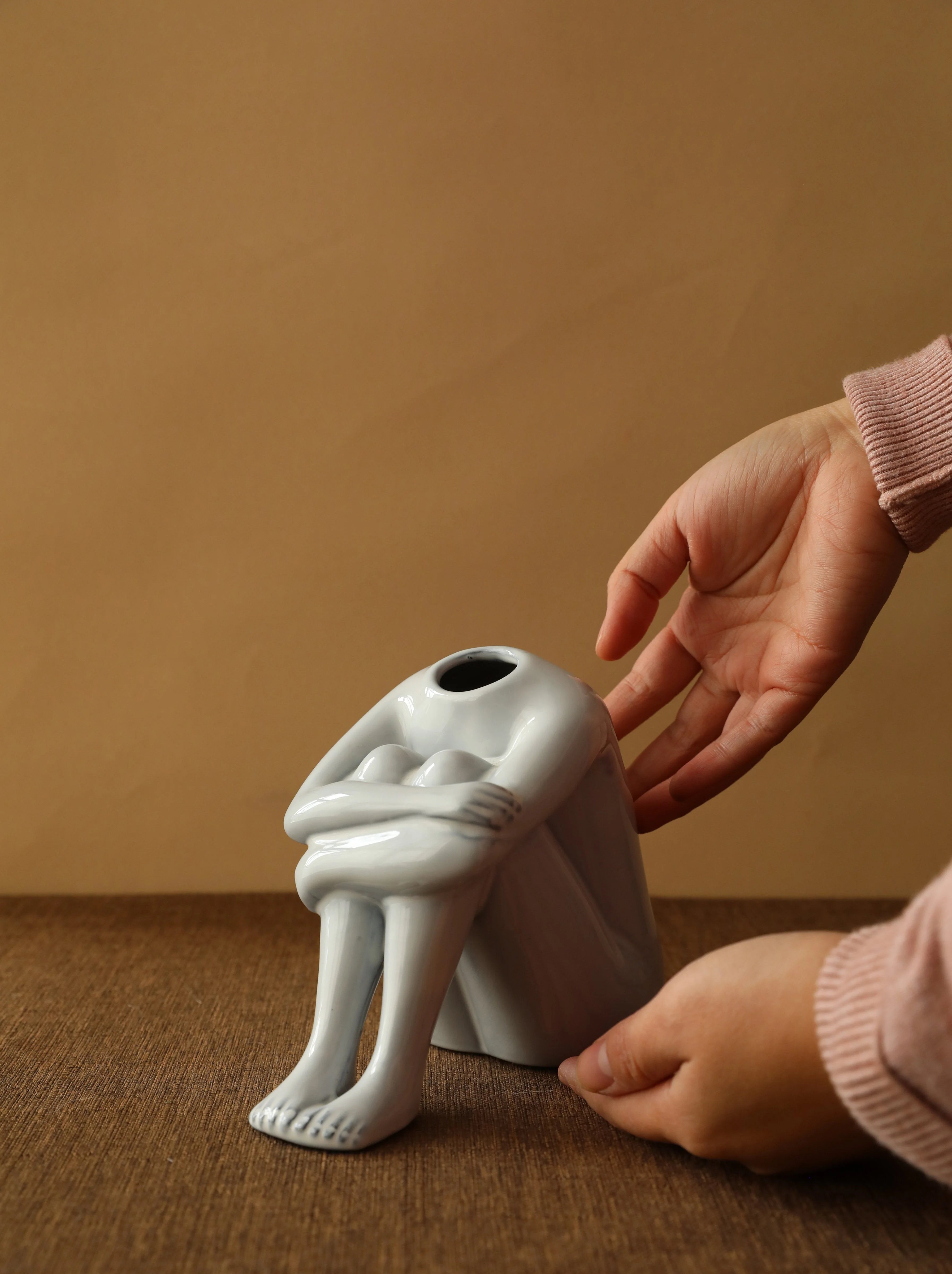 A hand placing the crouching figure ceramic vase on a wooden table. - RoomDen