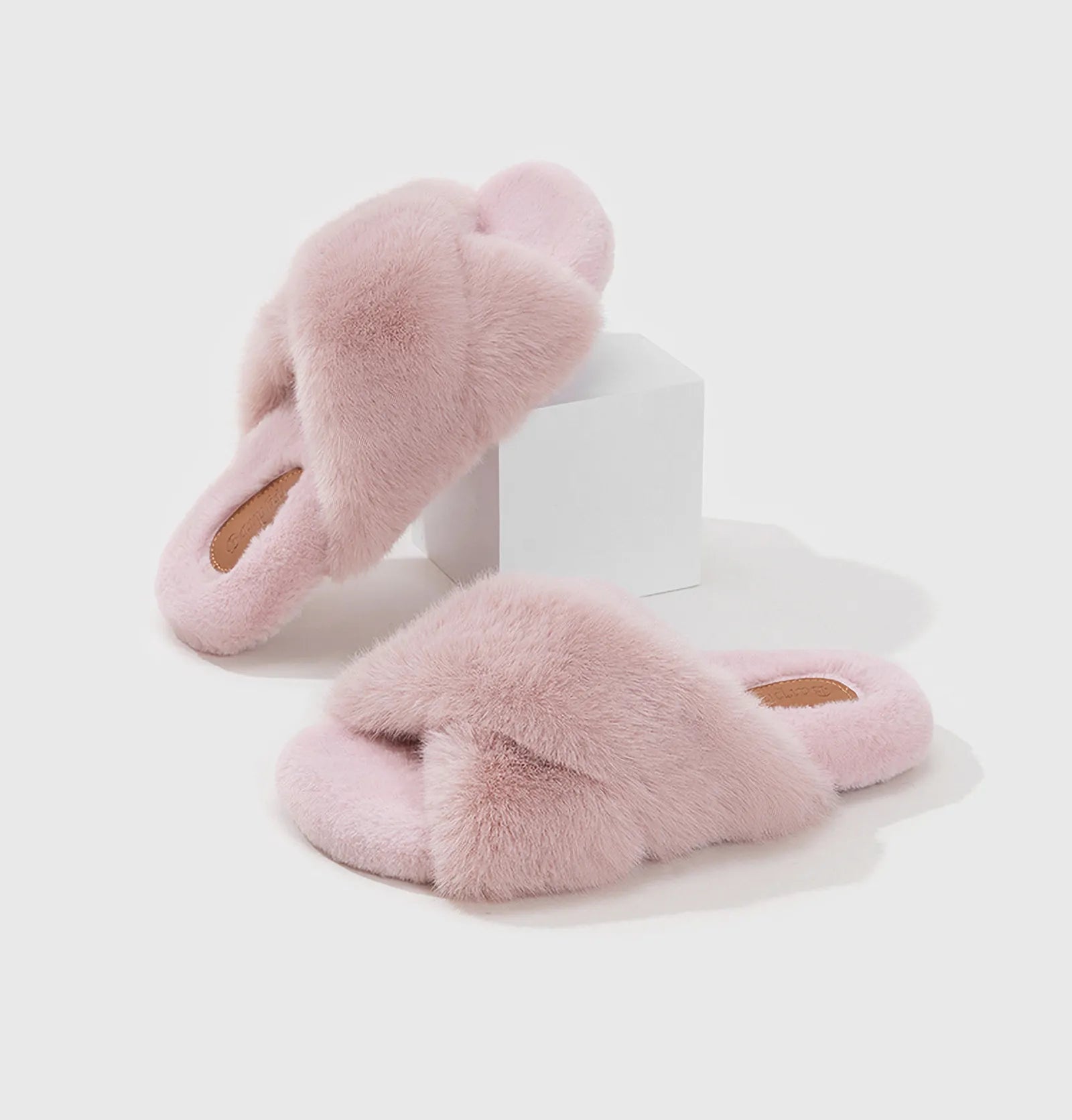 Pink plush slippers displayed on a white geometric block - RoomDen