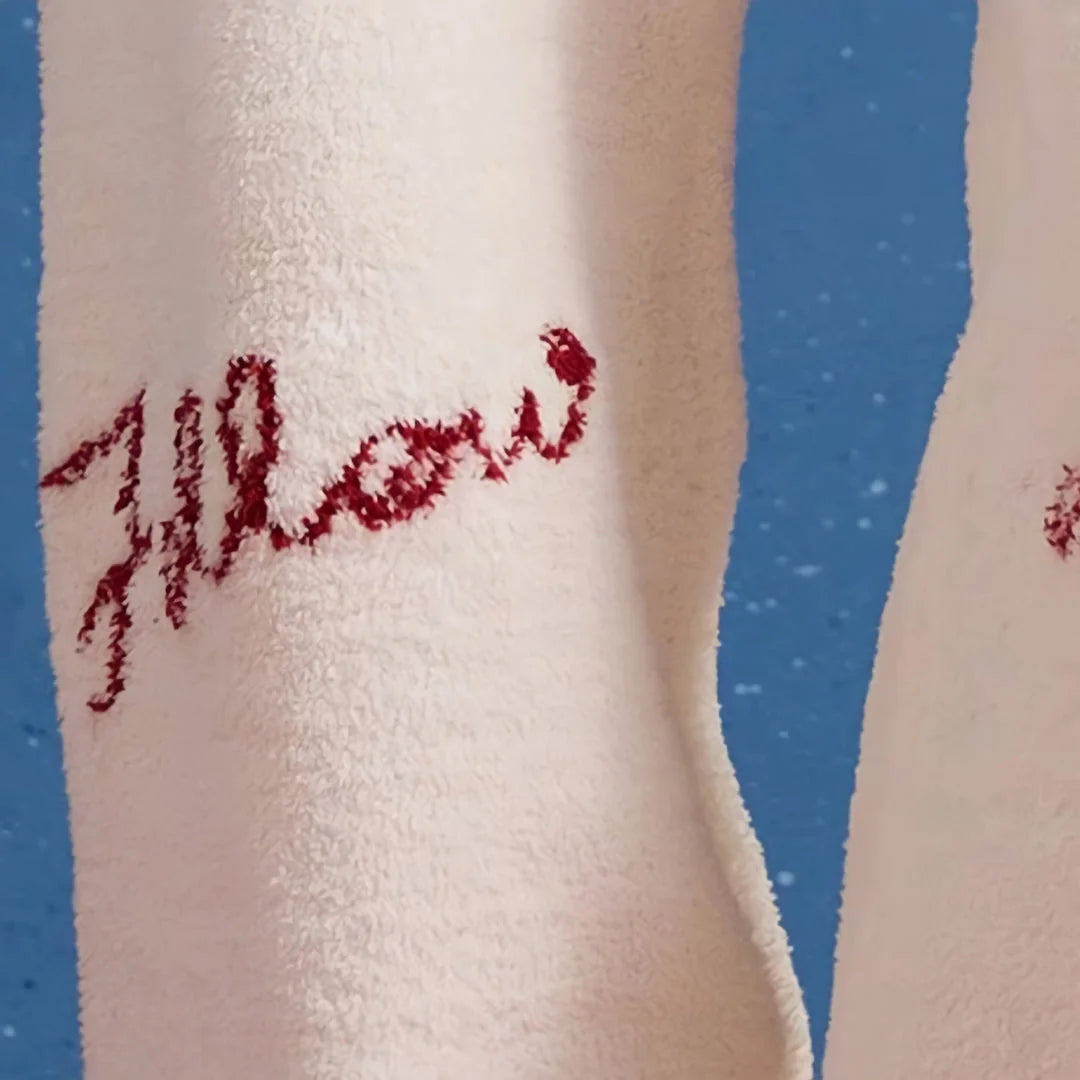 Macro shot of the red "Follow" script embroidered on the soft white flannel fleece fabric.