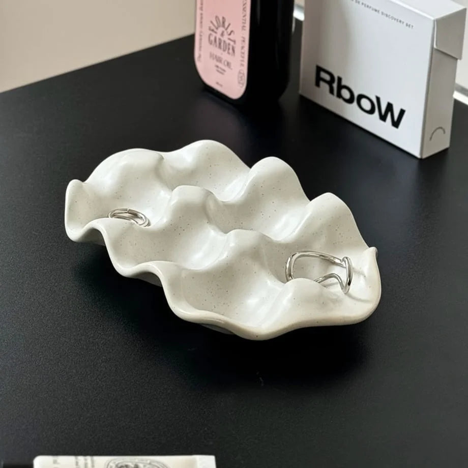 Speckled Wavy Ceramic Jewelry Dish in white holding two silver rings on a black desk. - RoomDen