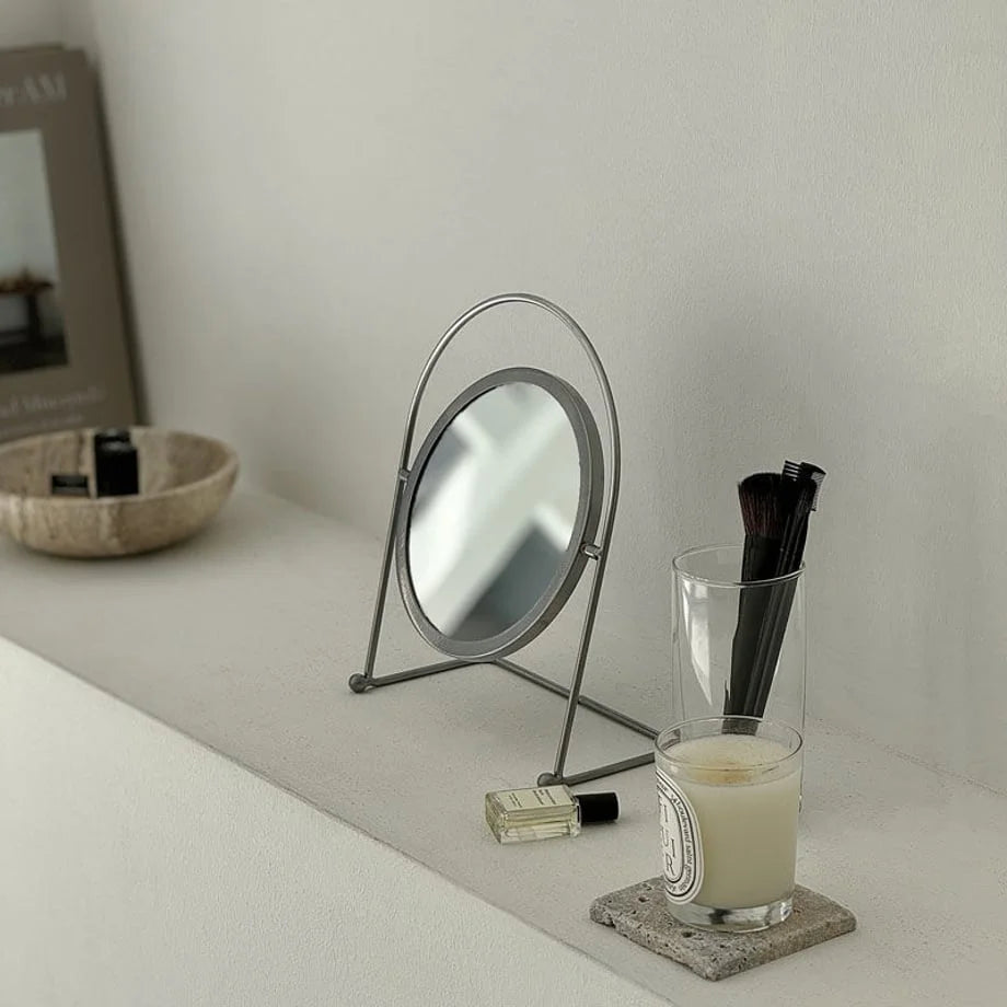 Japandi-style scene with the minimalist metal desktop mirror next to a candle and makeup brushes. - RoomDen