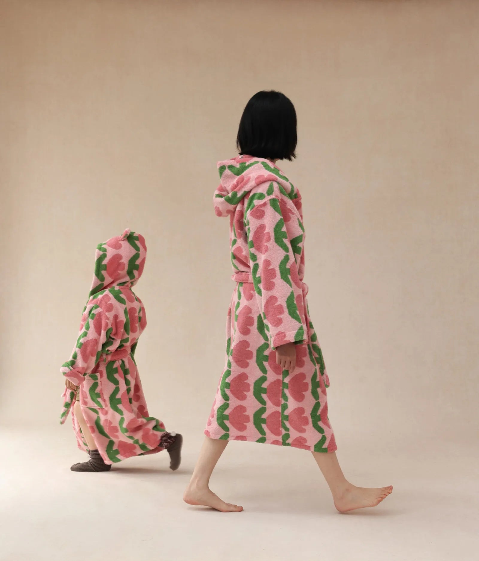 Back view of woman and child walking in matching pink and green tulip hooded robes - RoomDen.