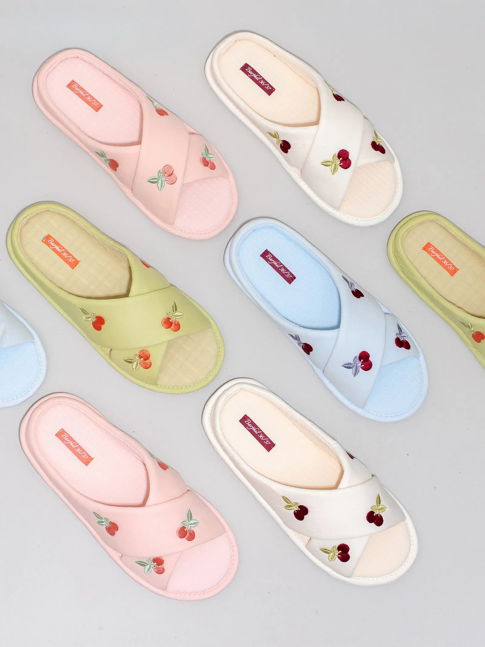Group flatlay of embroidered cherry slippers in pink, white, green, and blue - RoomDen
