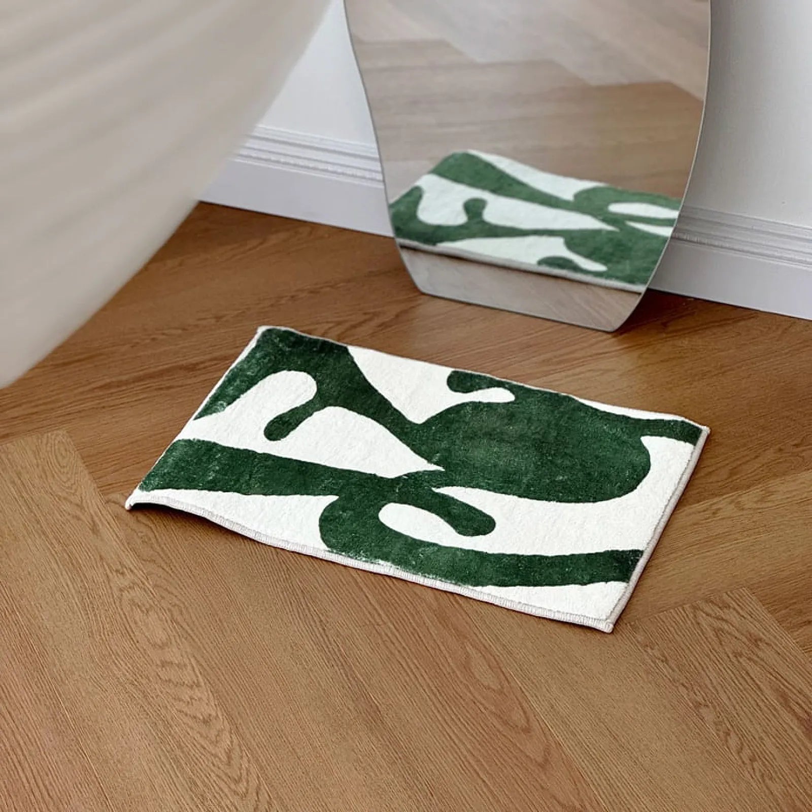 RoomDen forest green organic shape tufted rug placed in front of an irregular wavy mirror.
