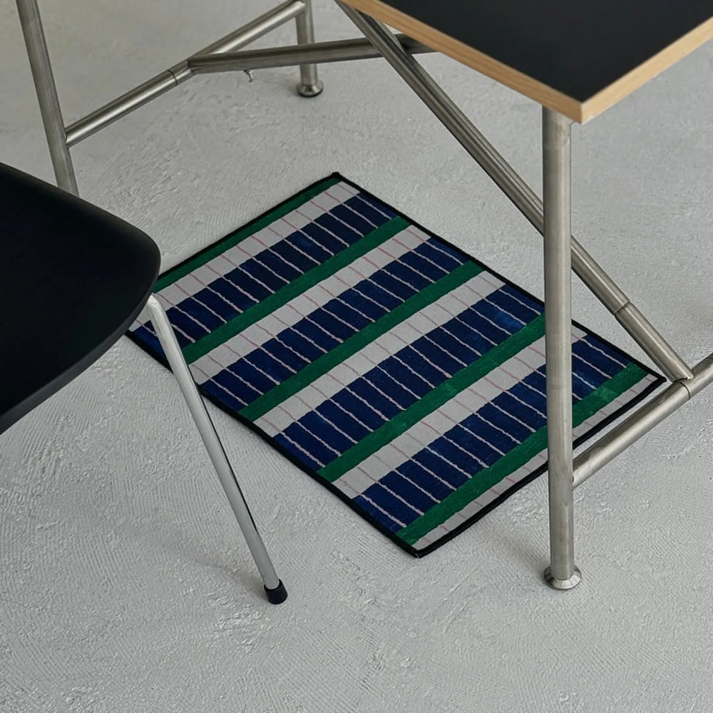 RoomDen modern piano key striped accent rug placed under a minimalist metal desk on a grey floor.
