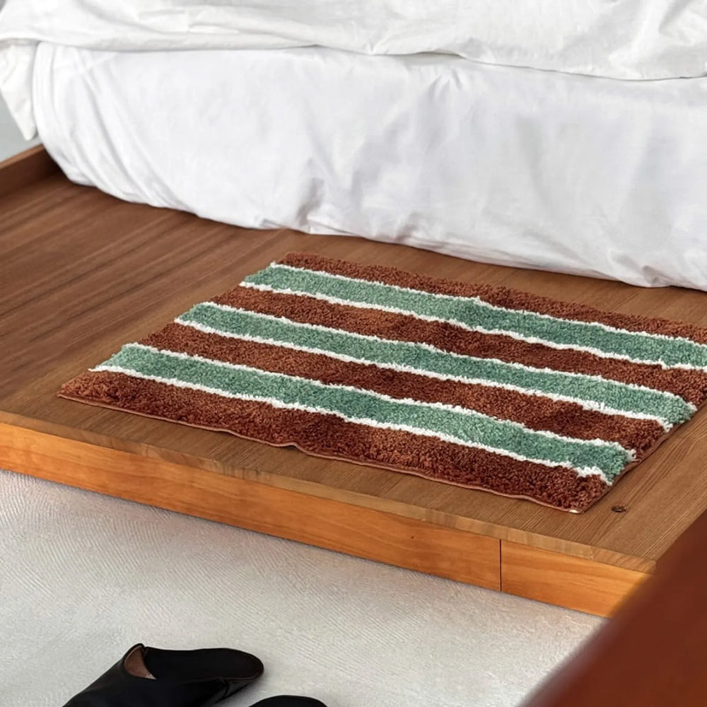 Angled view of a rectangular striped area rug placed next to a white bedding set.