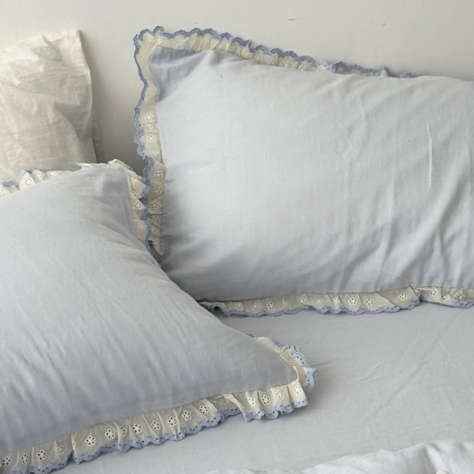 Two blue pillows with lace ruffles against white wall, soft natural lighting.