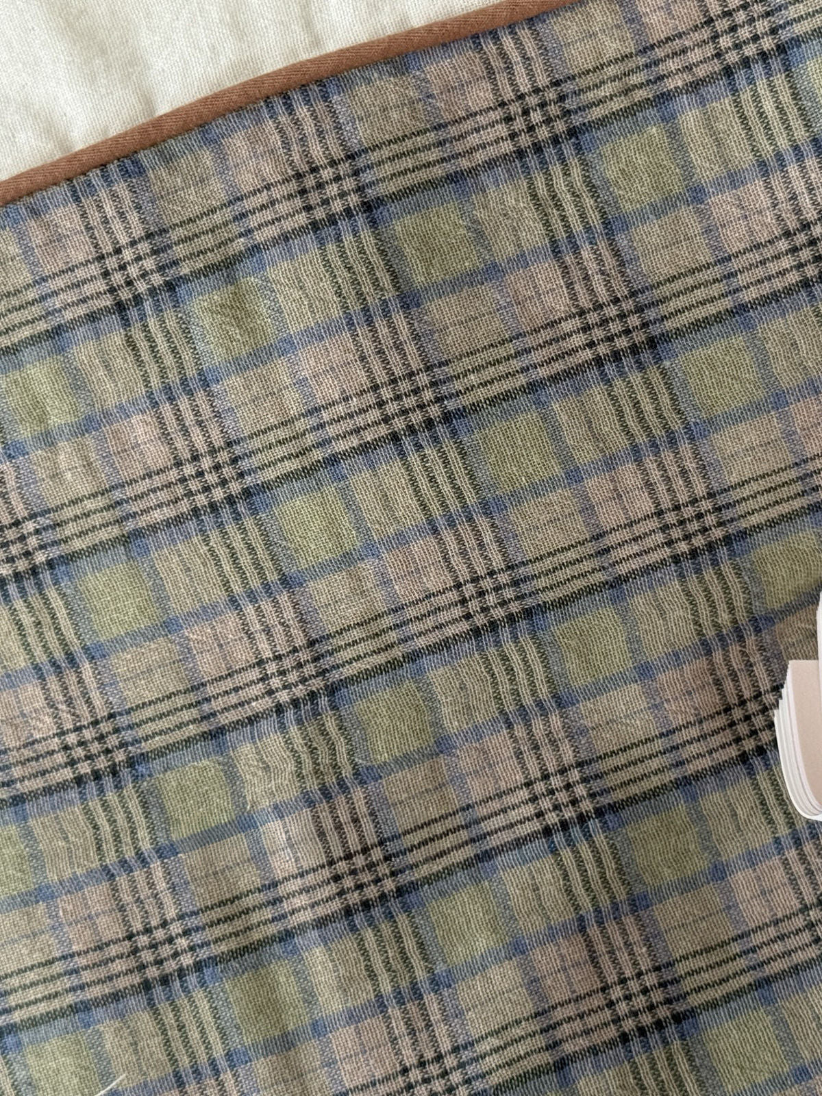 Detail shot of the sage green and brown plaid pattern texture on washed cotton fabric with piping. | RoomDen