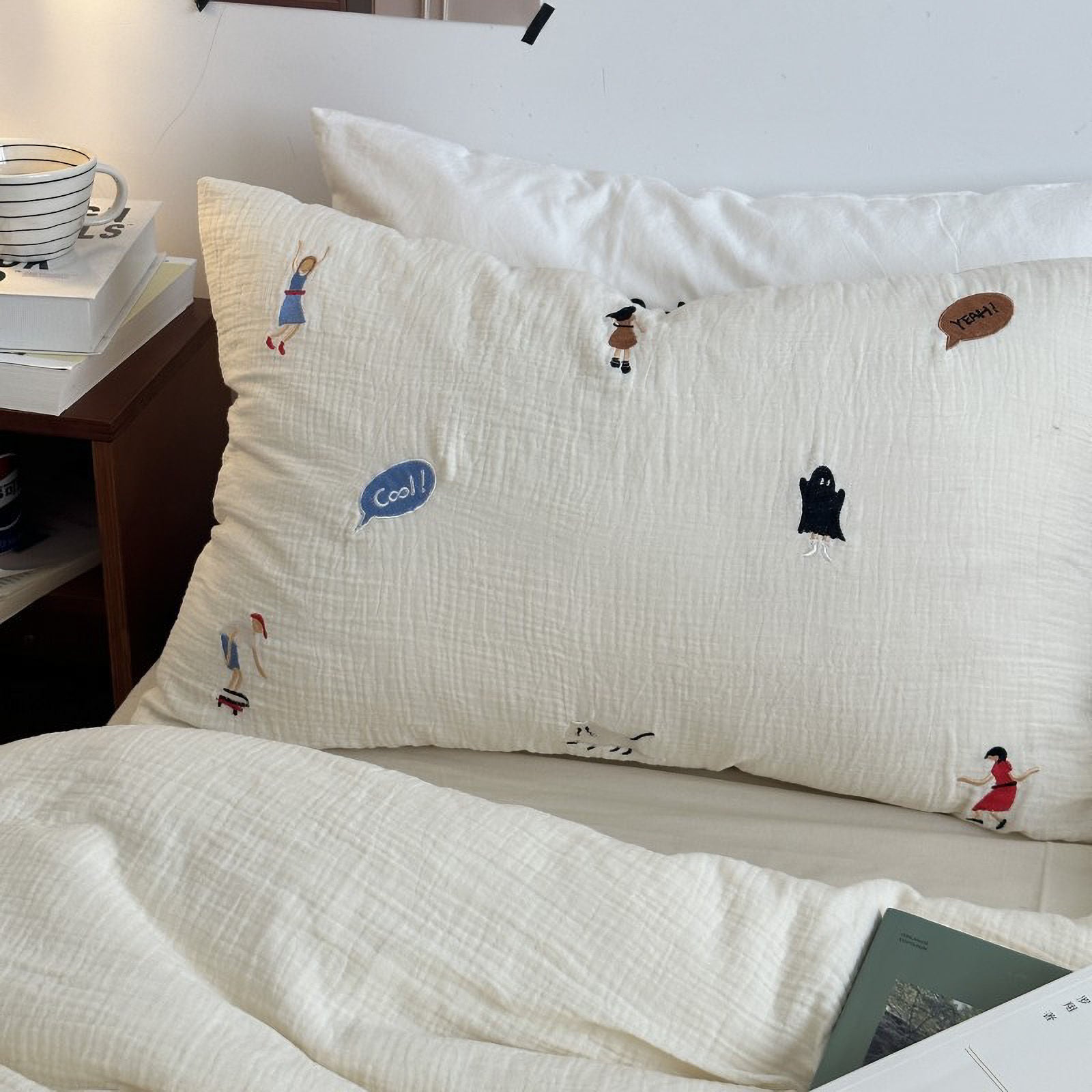 Close up of White cotton pillowcase with embroidered characters and "Cool!" bubble text.