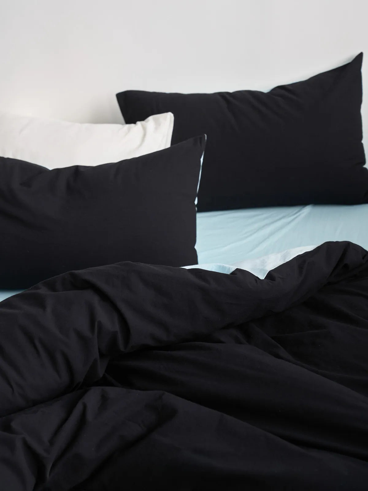 Close up of black and white pillows on a bed with black duvet cover and blue sheet RoomDen.