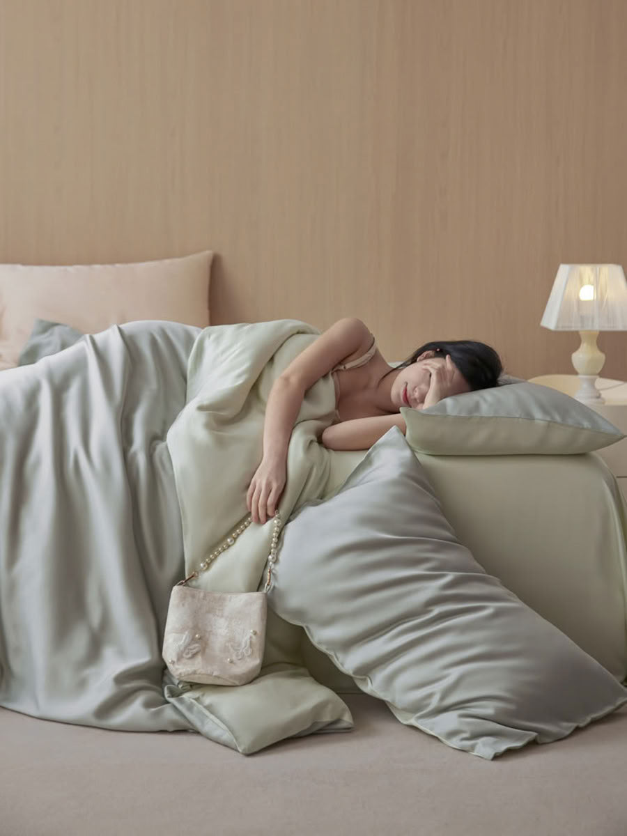 Soft mint green Tencel bedding draped naturally as woman relaxes in cozy bedroom – RoomDen