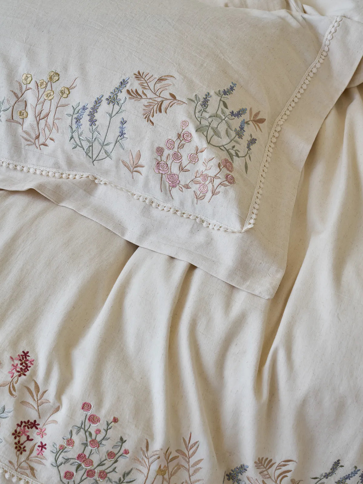 RoomDen linen pillowcase featuring intricate botanical embroidery and lace edge.