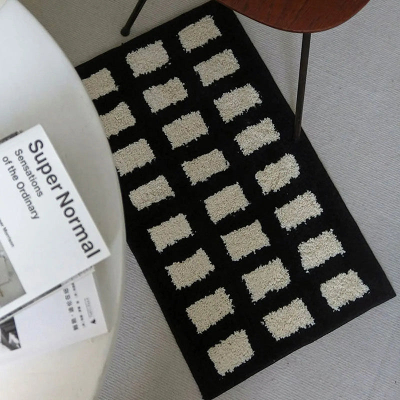 Top down view of black accent rug with cream tufted rectangular grid pattern - RoomDen