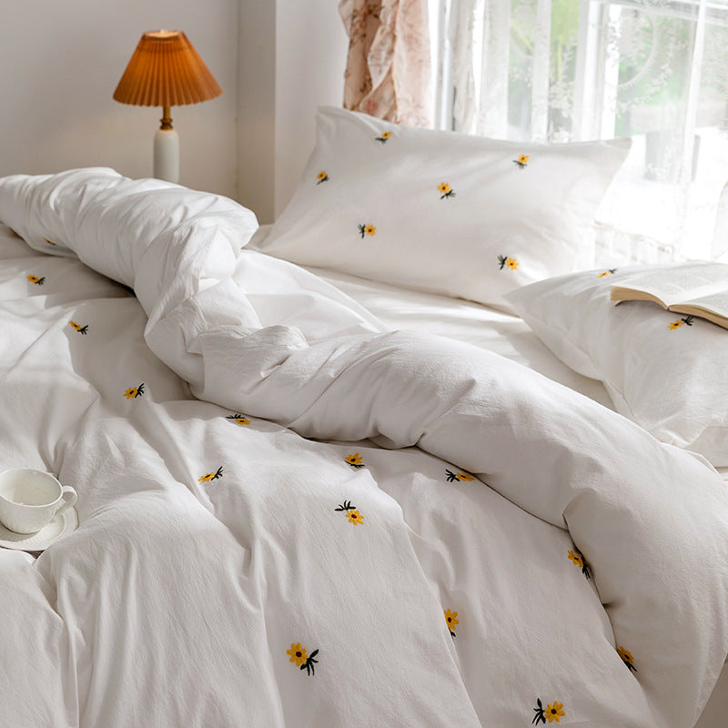 Daisy embroidered cotton bedding set – Side view of the floral duvet and pillows beside an amber lamp - Roomden