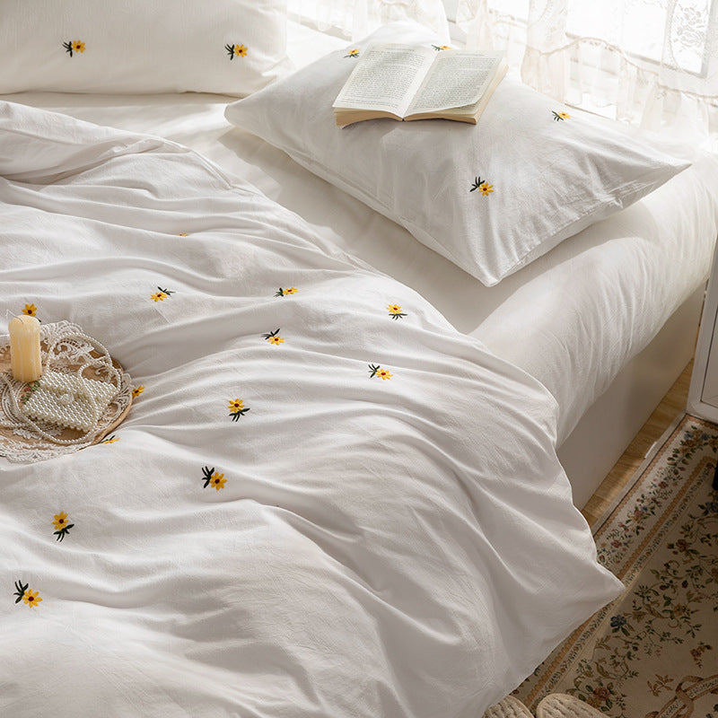 Daisy embroidered cotton bedding set – Overhead view of the ivory duvet, pillows and small floral motifs - Roomden