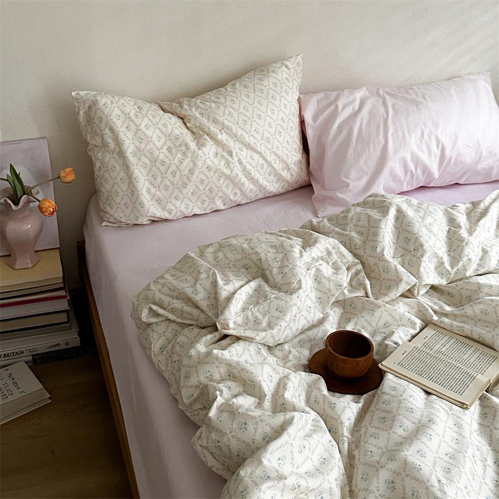 Ivory floral lattice cotton bedding with a pale pink accent pillow, shown on a bed - Roomden