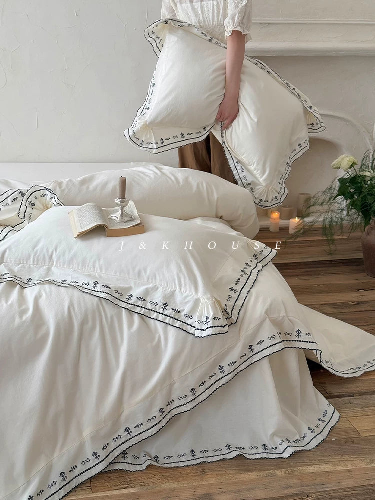 Scalloped embroidered washed cotton bedding set – Ink White, pillowcase held above the bed - Roomden