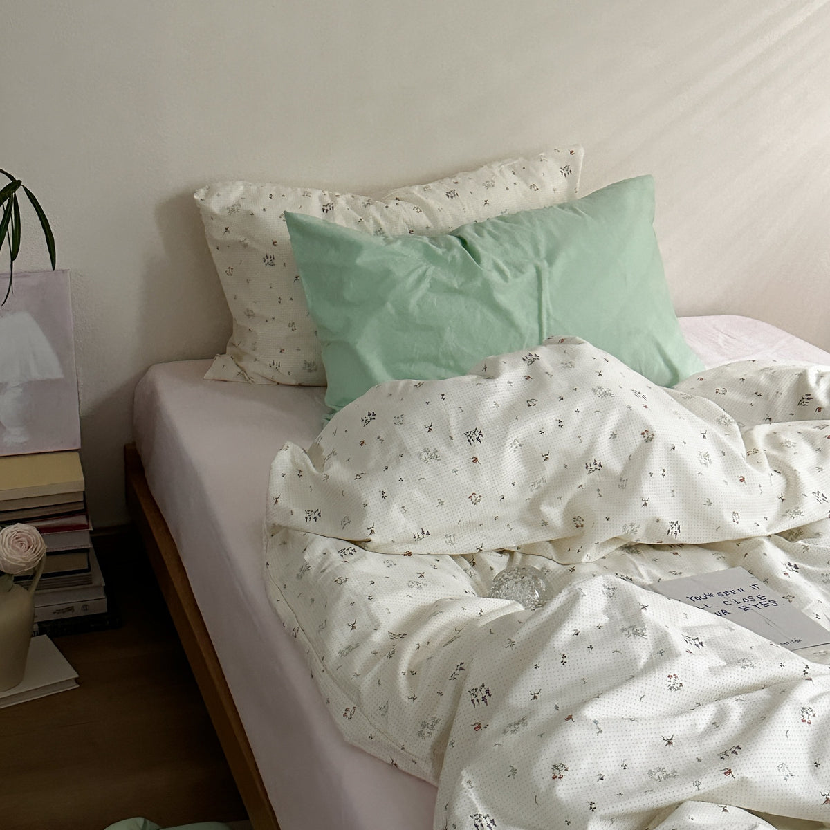 Ivory cotton bedding with small botanical motifs and a mint green accent pillow, shown on a bed - Roomden
