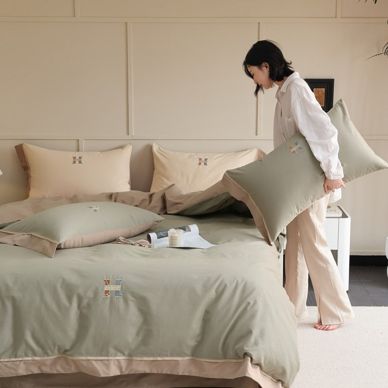 Sage green cotton bedding with beige borders and small embroidered motifs in a bedroom - Roomden