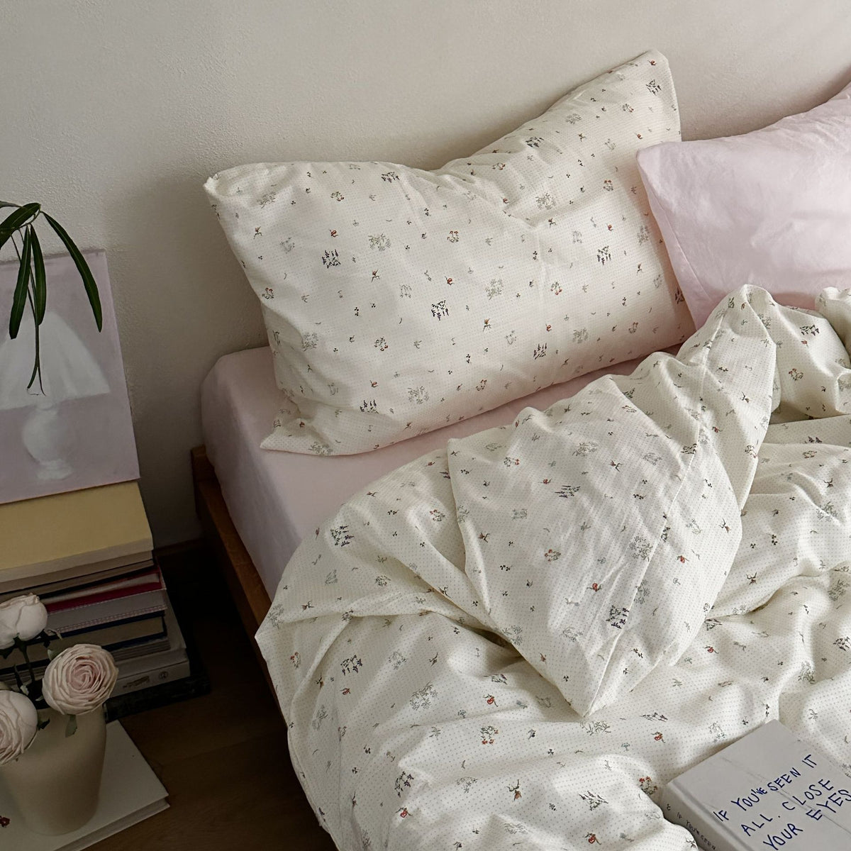 Ivory cotton bedding with small botanical motifs and a pale pink accent pillow, shown on a bed - Roomden