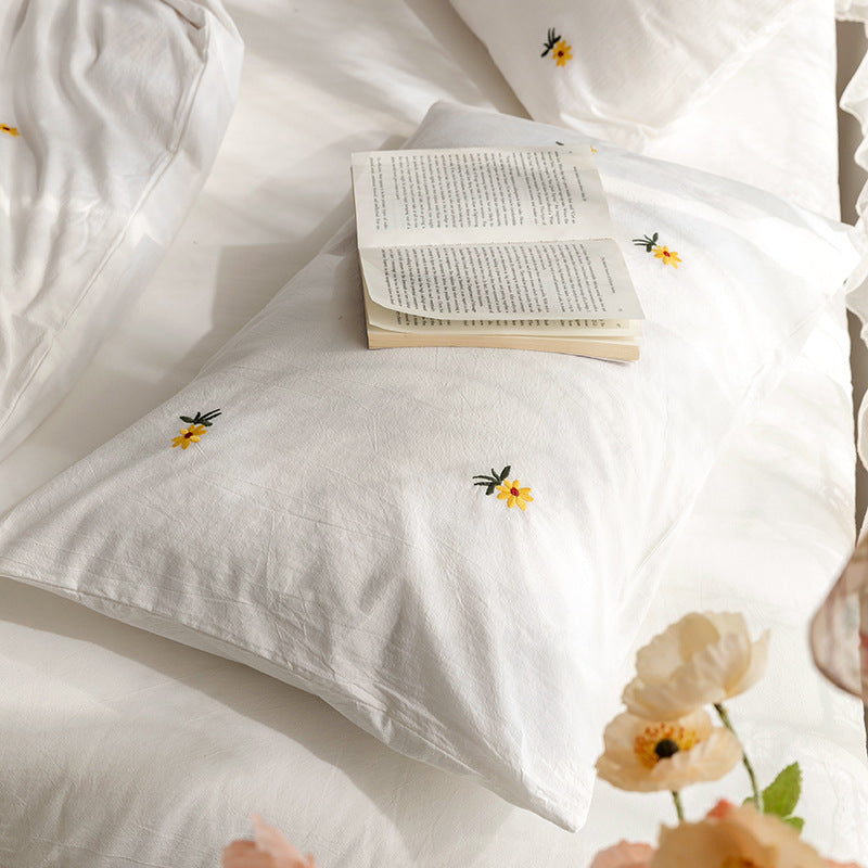 Daisy embroidered cotton bedding set – Close view of embroidery beside an open book - Roomden