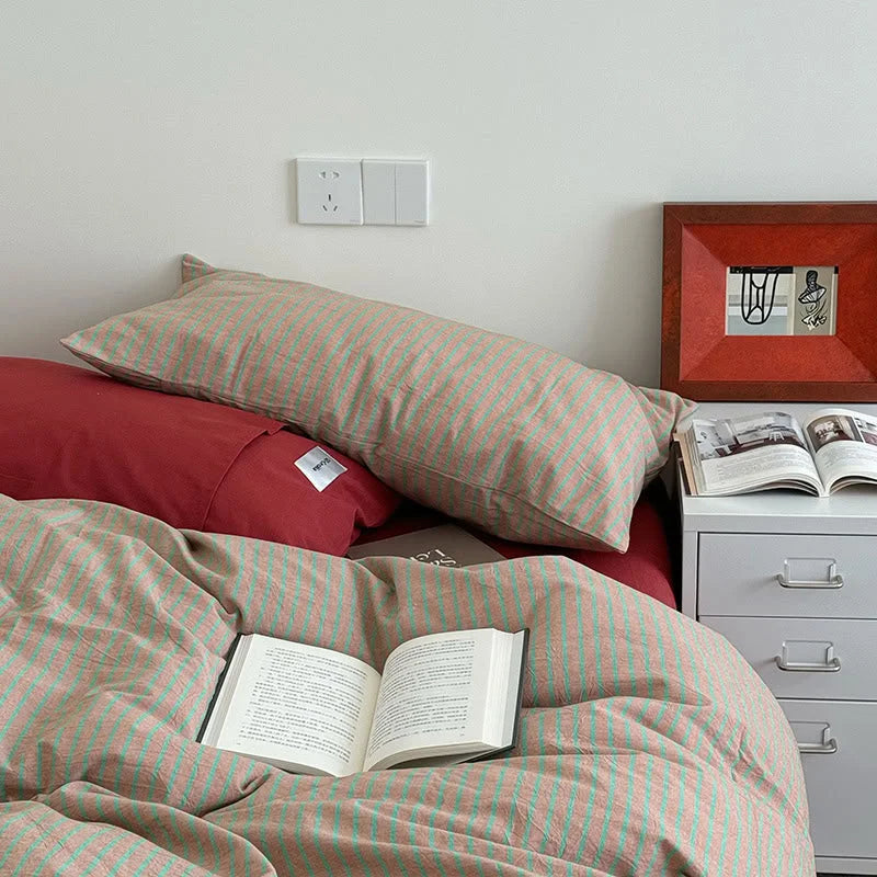 Close-up of a cozy bed with Red & Green Striped Washed Cotton Bedding, with an open book resting on the duvet - RoomDen.