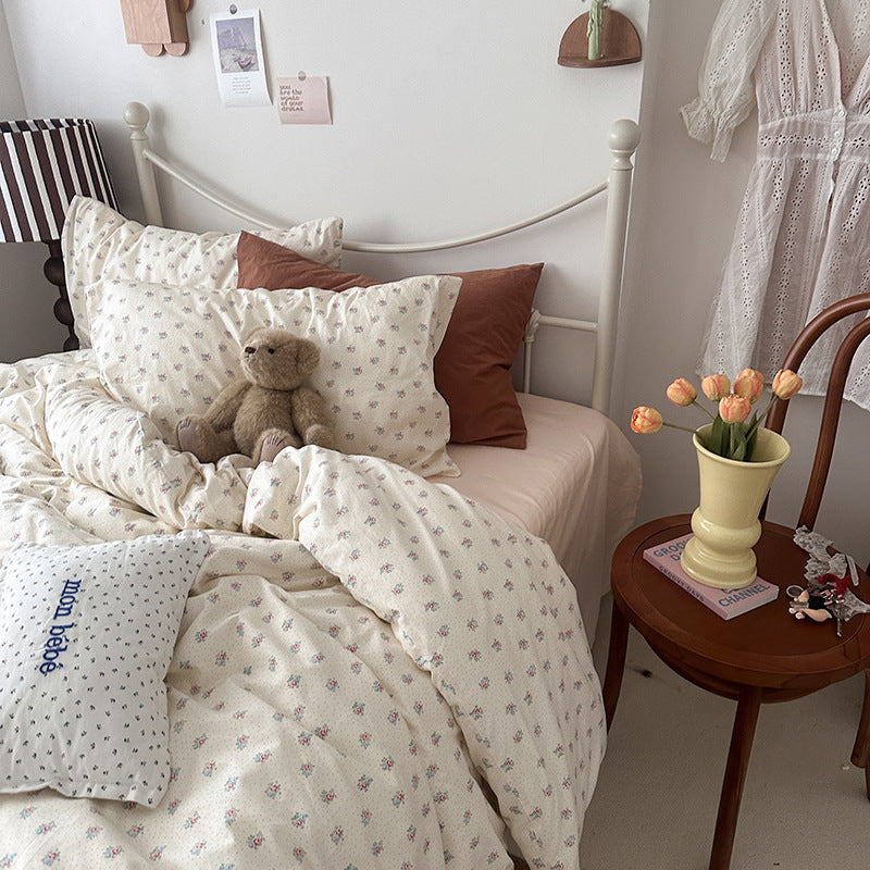 Ivory rosebud cotton bedding set with tiny pink flowers and green leaves, shown on a cream metal bed - Roomden
