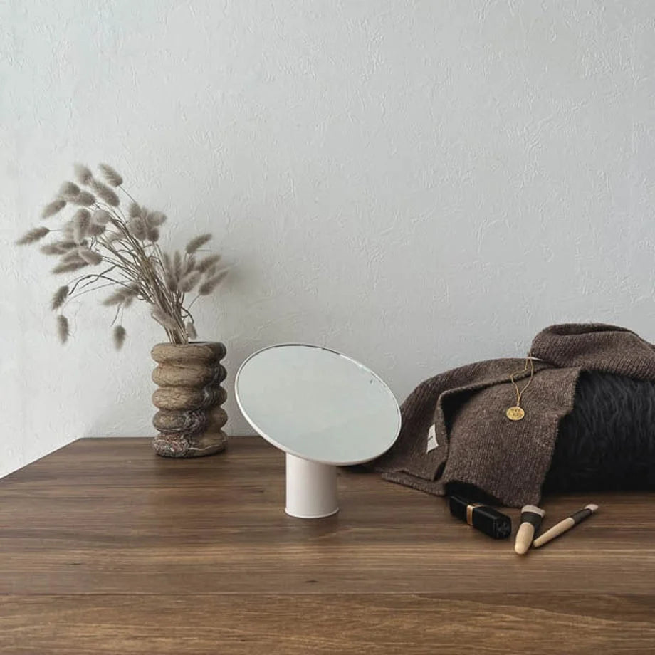 The white Japandi-style desktop mirror next to a textured vase with dried flowers.