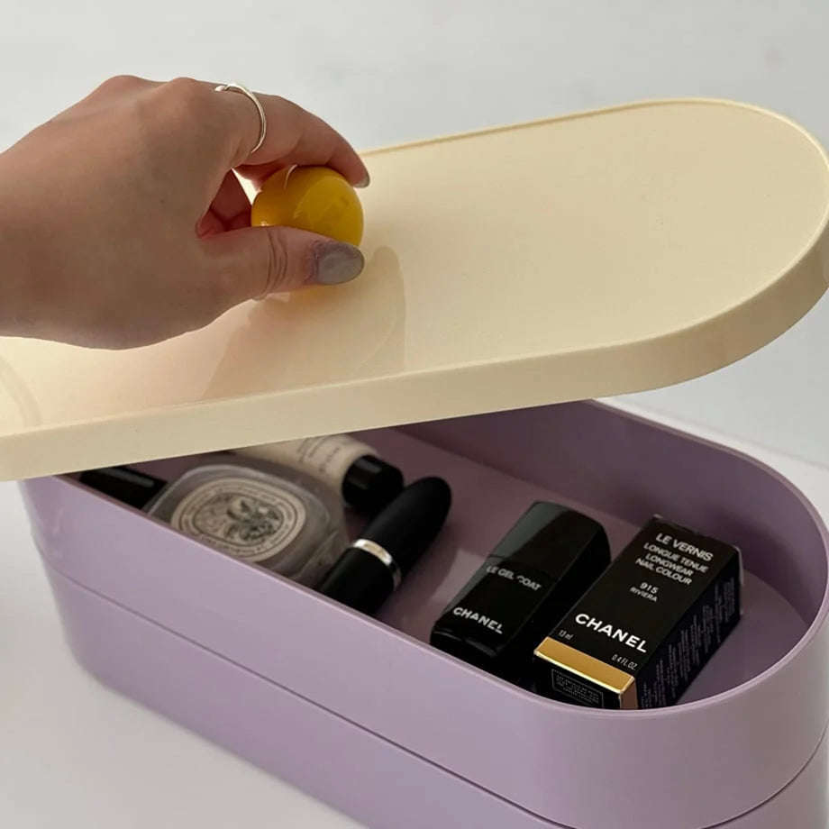Hand lifting the cream lid by its yellow knob to reveal cosmetics stored inside the lavender organizer.