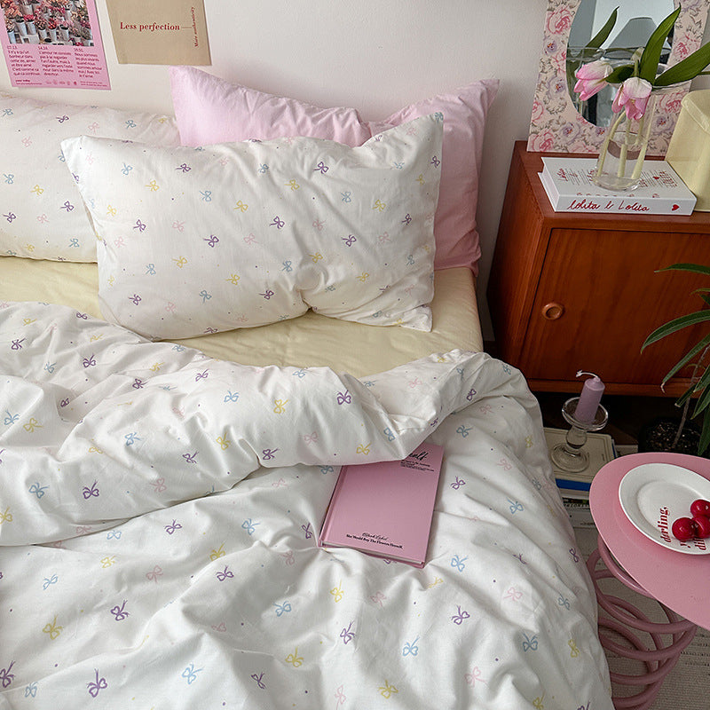 Ivory pastel bow cotton bedding – colorful small bows and pink pillow styling beside a wooden bedside table - Roomden