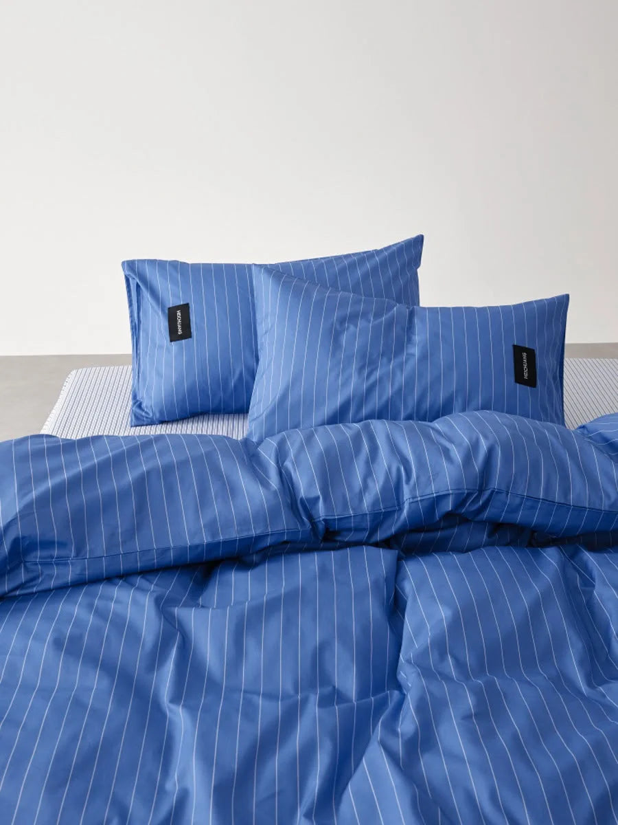 Detail shot of the two Denim Blue Pinstripe pillowcases and duvet cover, showing the black RoomDen label - RoomDen.