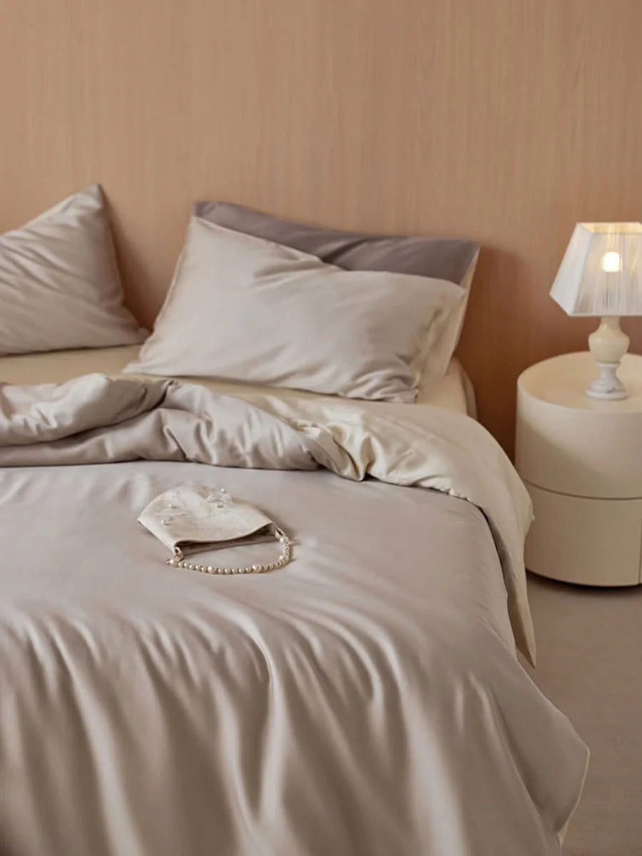 The Oat Milk Tencel bedding set neatly made on a bed next to a modern white nightstand and lamp. - RoomDen