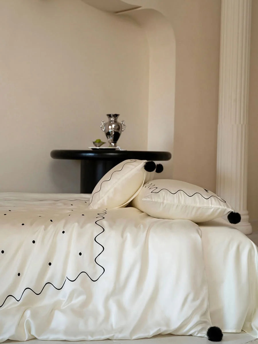 Detail shot of the Creamy White & Black Tencel bedding set in a room with a black side table and column. - RoomDen