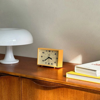 Angled view of the Mustard Yellow Retro Table Clock on a wooden surface with books.